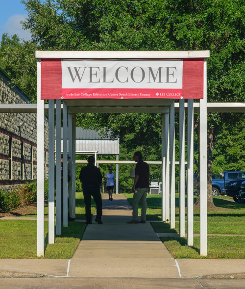 Three people in shadows stand underan outdoors covering at the Liberty campus, a welcome banner overhead