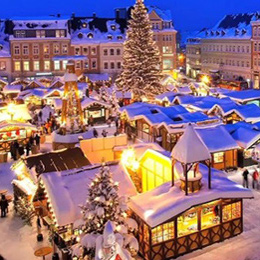 A quaint town square at dusk coverd in snow and lights, with a large Christmas tree